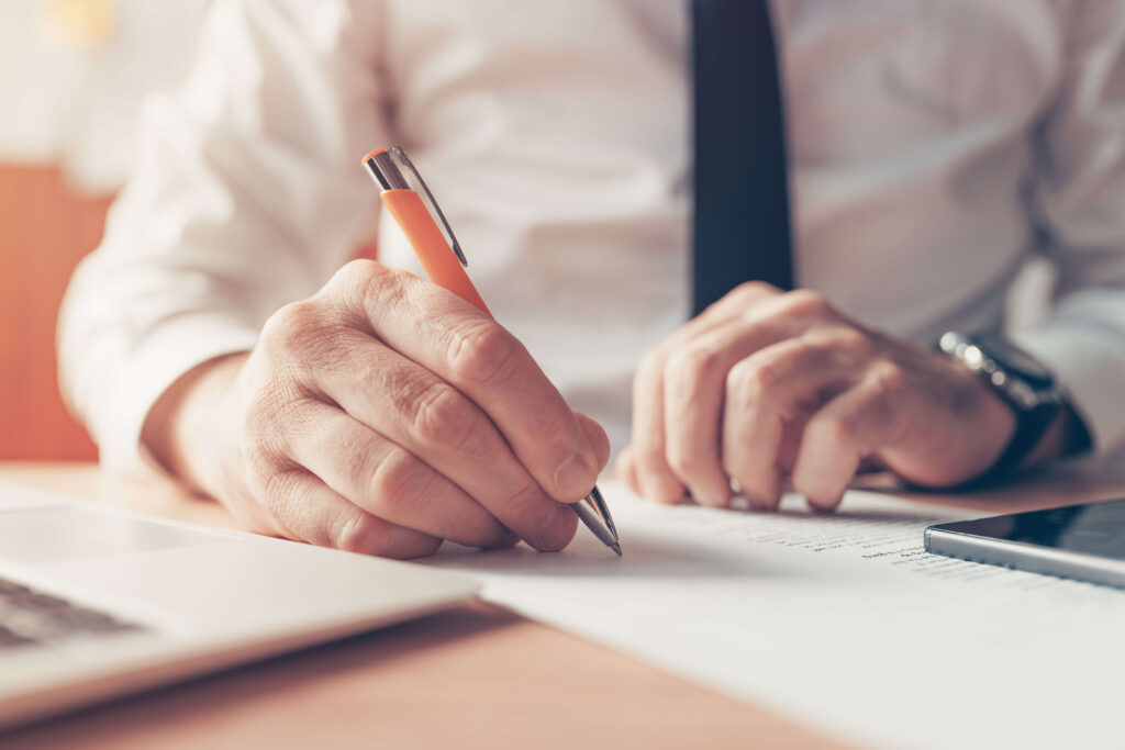 homme en costume remplissant un document avec un stylo orange